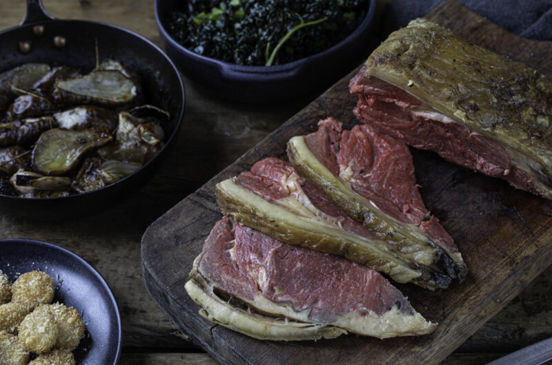 Bone-in sirloin roast sliced on a wooden board with Jerusalem artichokes, shallots, cavolo nero and crispy bone marrow balls