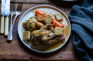 A plated dish of roast partridge with smoked lardons, caramelised apples, and a glossy brandy sauce