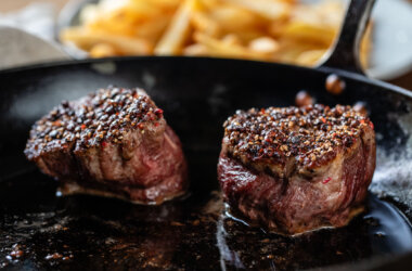 Two grass-fed fillet steaks searing in a cast iron pan, developing a rich, caramelised crust