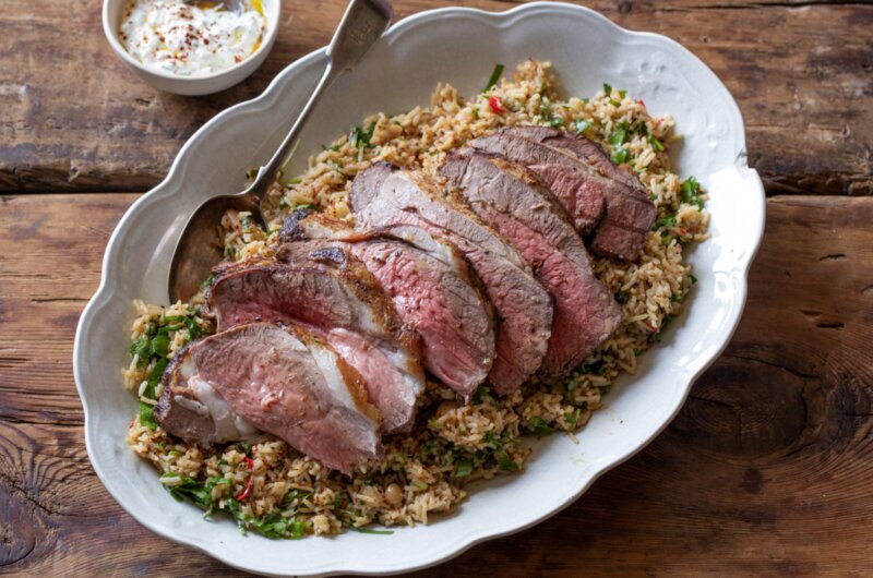 Butterflied leg of lamb cooked pink, sitting on top of rice pilaf and served with a minted yoghurt dip.
