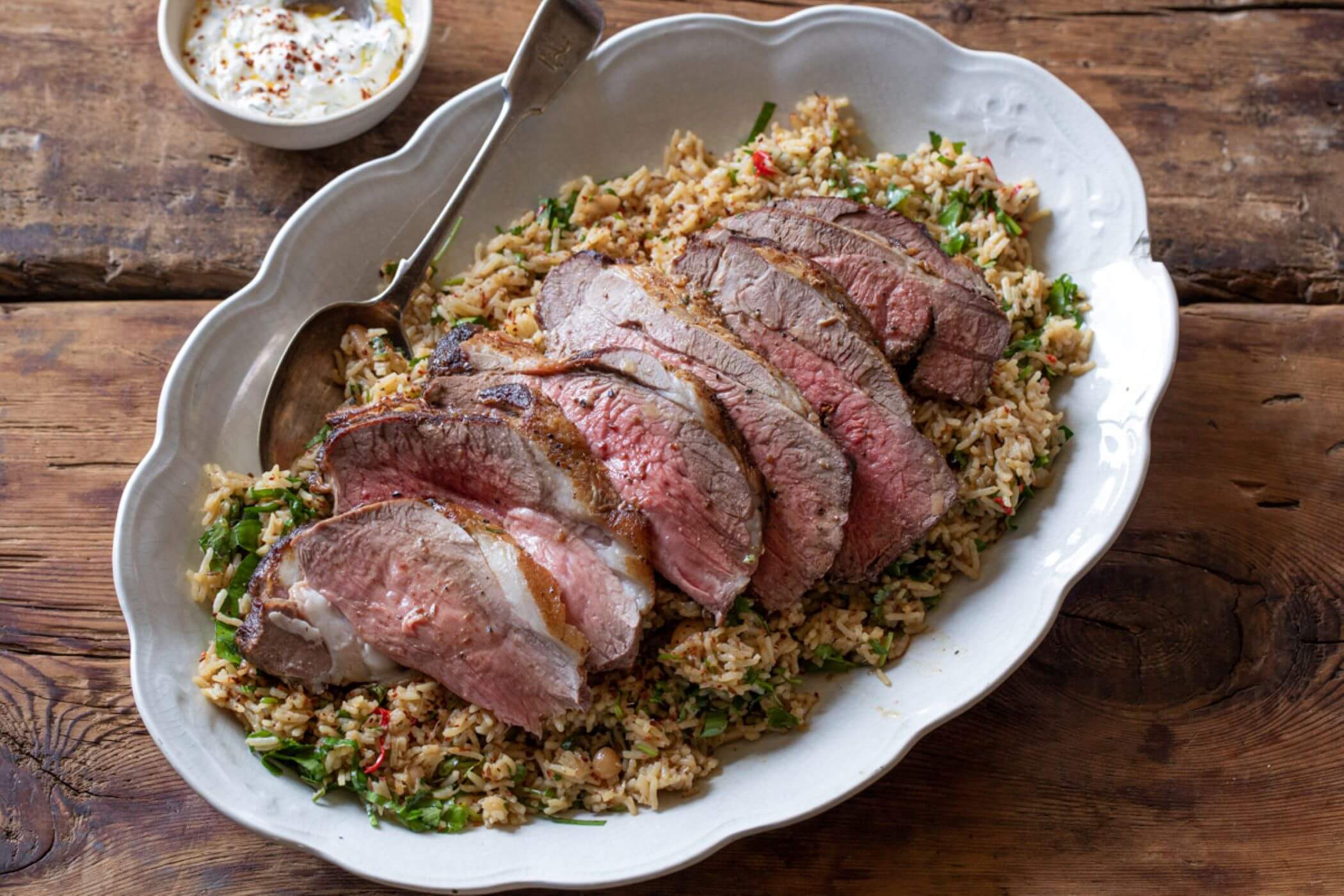 Butterflied leg of lamb cooked pink, sitting on top of rice pilaf and served with a minted yoghurt dip.
