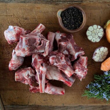 Lamb bones alongside carrots, black peppercorns, and a chopped onion.