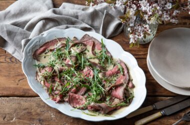 Close-up of rare roast topside of beef with tonnato dressing served in a white serving dish.