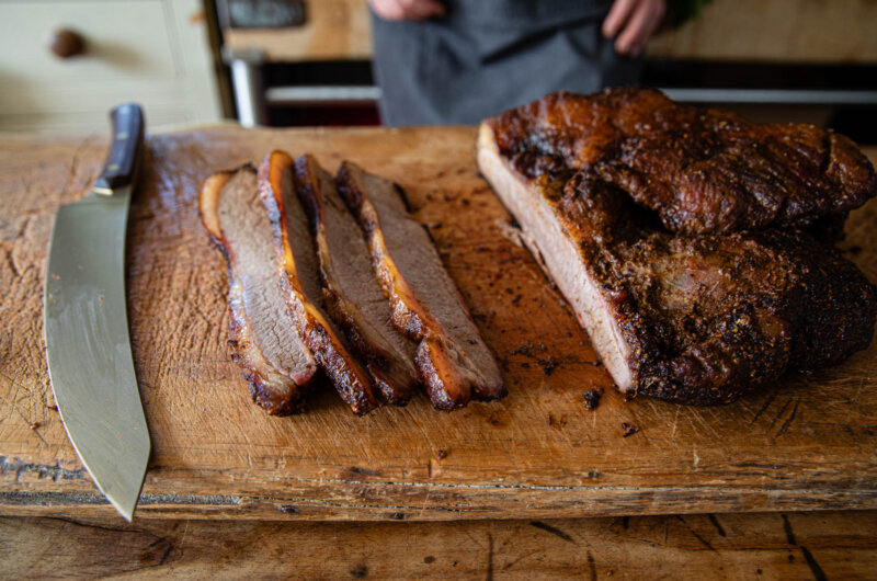 Sliced smoked brisket on a wooden board with the remaining brisket ready to carve
