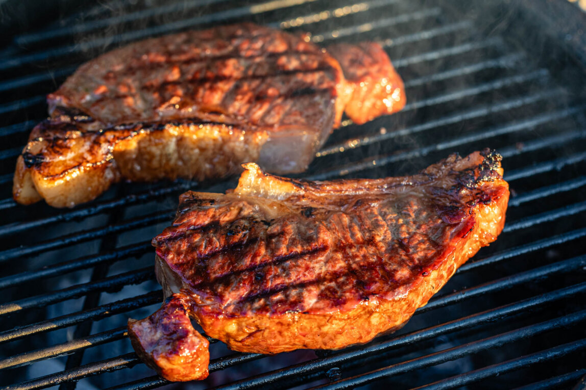 Two sirloin steaks cooking on a barbecue grill, heritage breed beef with rich marbling, seared over hot coals for smoky flavour