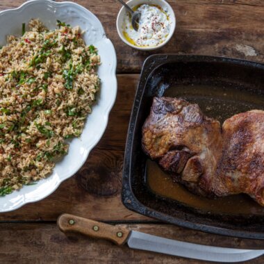 Rice pilaf salad in a white serving dish next to butterflied leg of lamb.