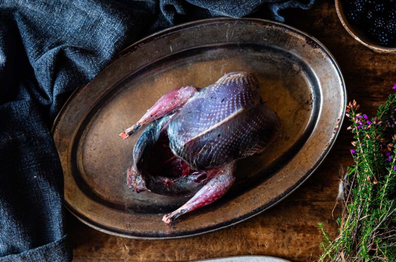 A raw whole grouse on a serving plate.