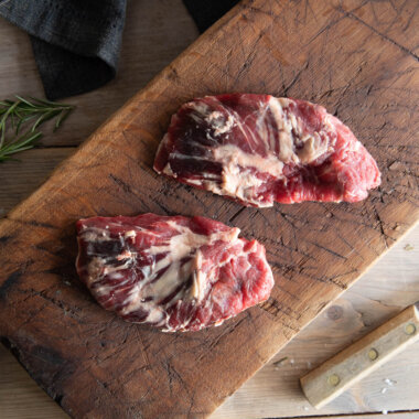 Bird's eye view of raw spider steaks on a wooden board with rosemary and a knife either side.