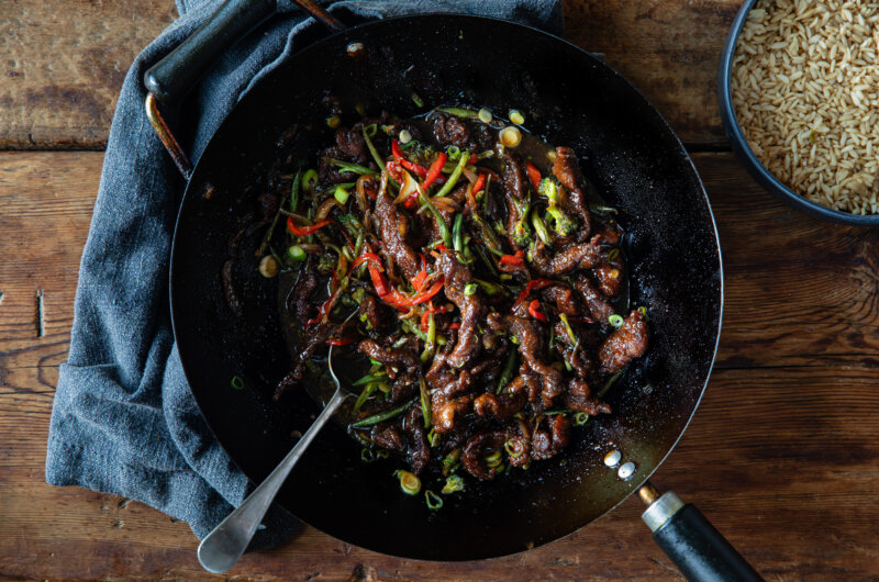Overhead shot of Mongolian beef stir fry in a wok with a bowl of steamed rice to the side.