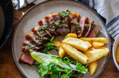 Bird's eye view of sliced steak, chips and salad on a plate dressed with chimichurri.