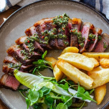 Bird's eye view of sliced steak, chips and salad on a plate dressed with chimichurri.