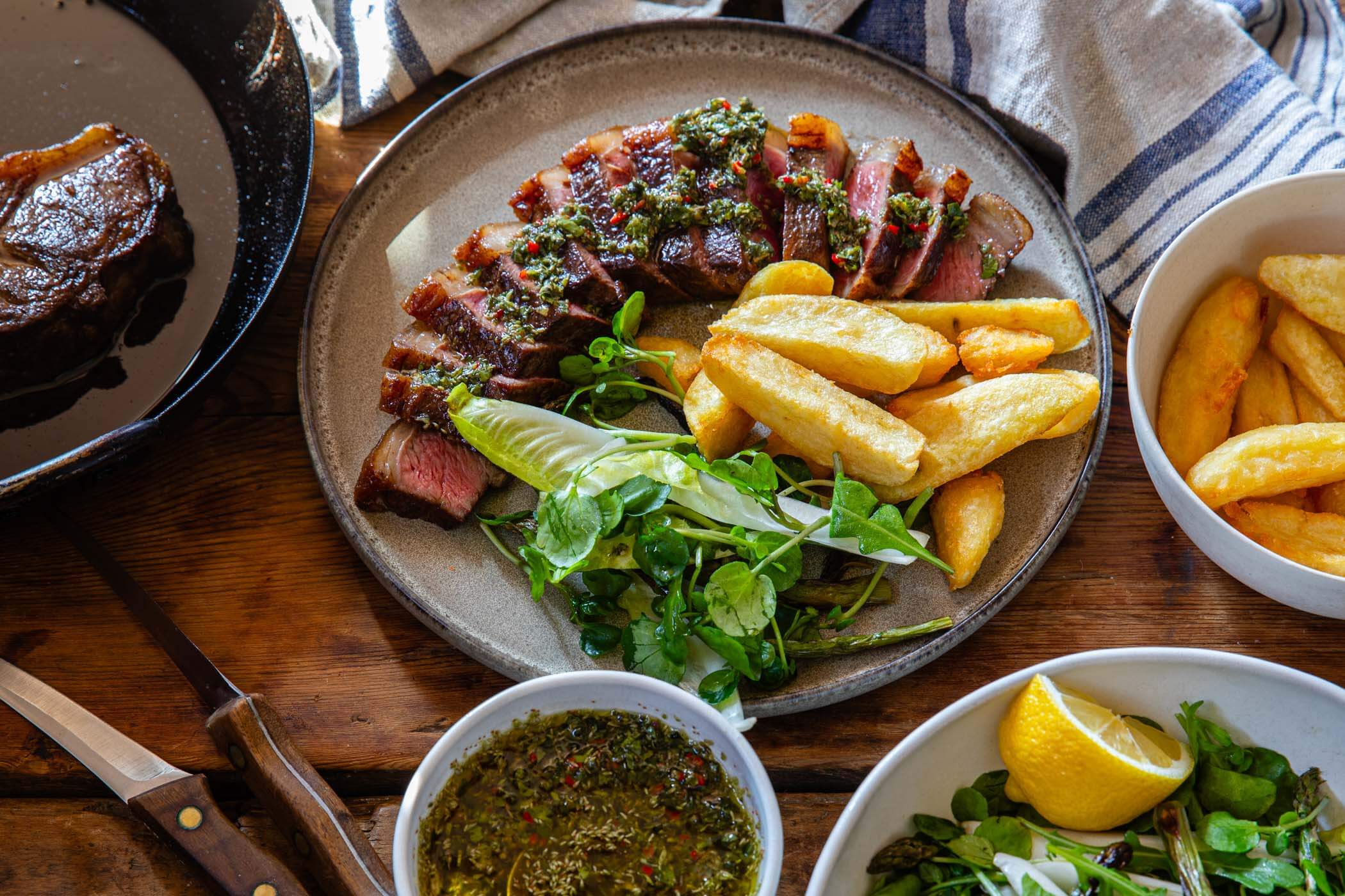 Chimichurri sauce spooned over sliced grilled steak with French fries on a plate