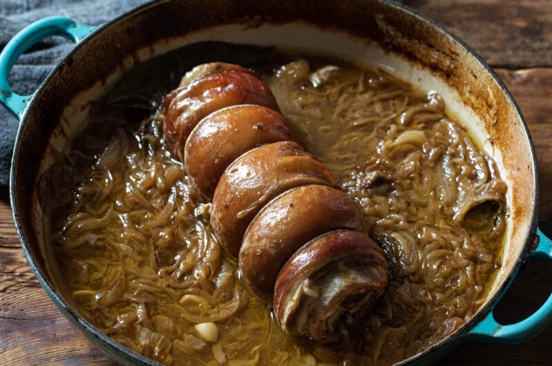 A braised, rolled belly of lamb and onions in a casserole dish.