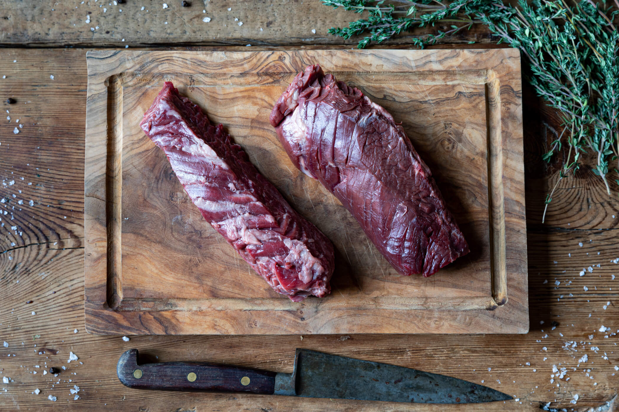 An overhead picture of two onglet steaks on a wooden chopping board, with a knife laying parallel to the board.
