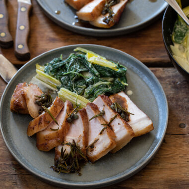Pork loin sliced on plate with Swiss chard, pan of Swiss chard to the right with spoon in