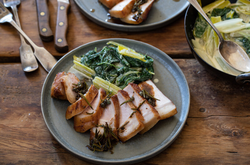 Pork loin sliced on plate with Swiss chard, pan of Swiss chard to the right with spoon in