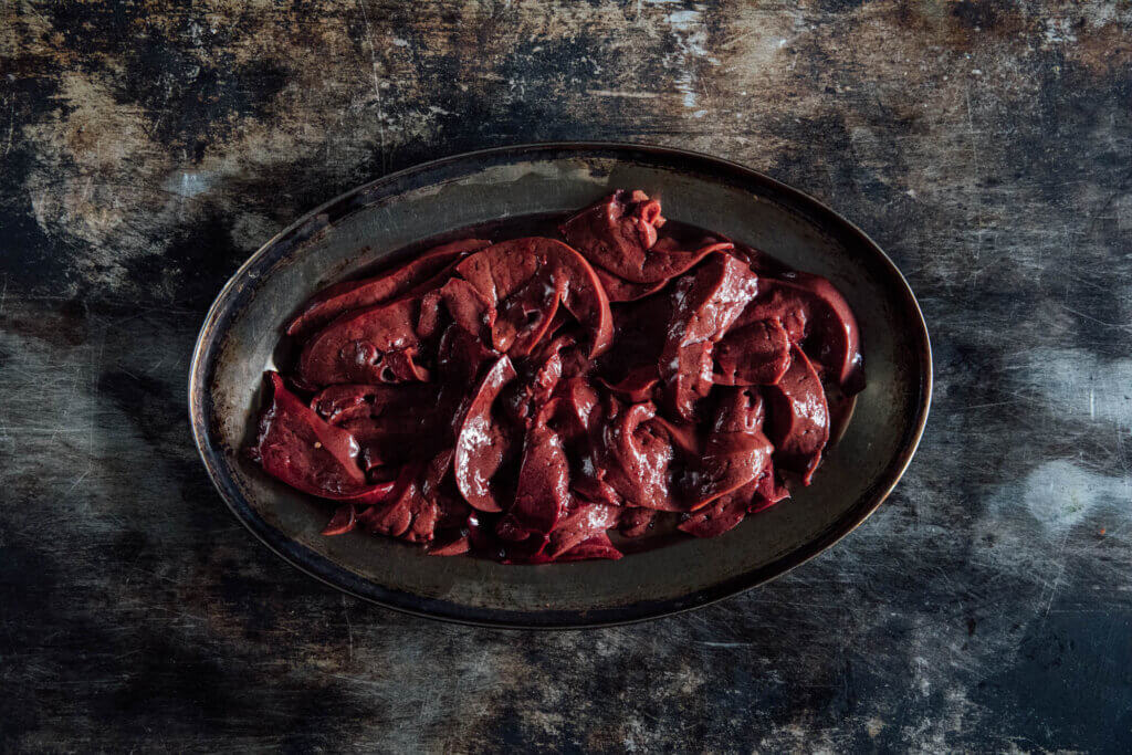 An overhead shot of sliced lamb's liver on an oval metal tray. 