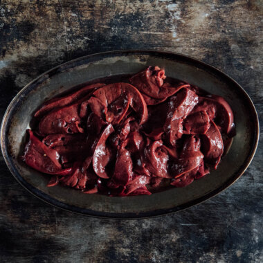 An overhead shot of sliced lamb's liver on an oval metal tray.
