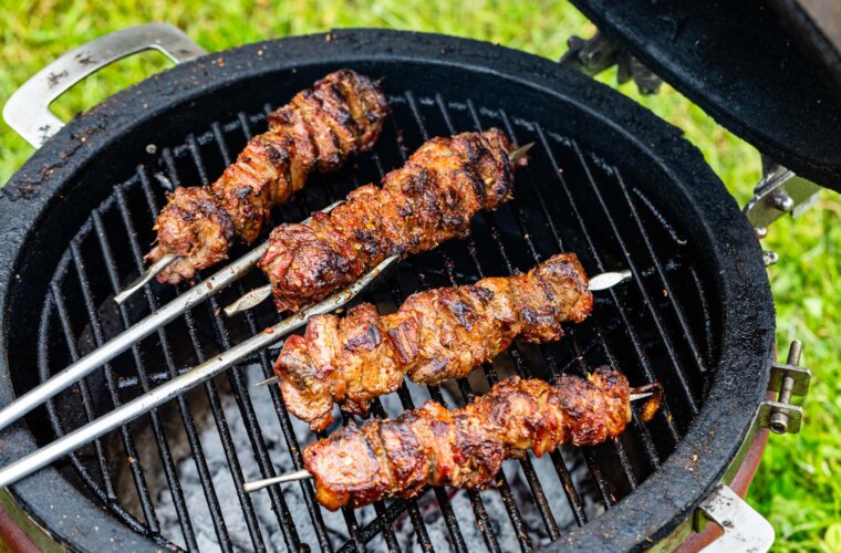 Four lamb skewers cooking over hot coals on a barbecue grill