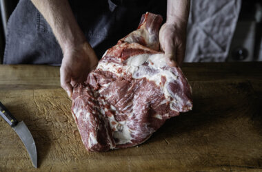 Raw whole mutton shoulder on a wooden board, ready for slow cooking