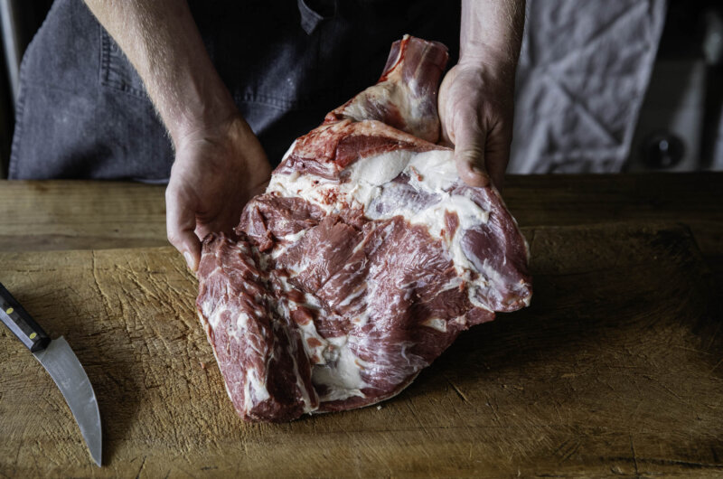 Raw whole mutton shoulder on a wooden board, ready for slow cooking