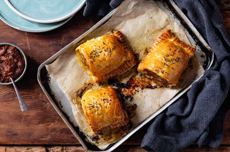 Golden curried sausage rolls freshly baked, with flaky pastry and a rich, spiced filling, served on a rustic baking tray.