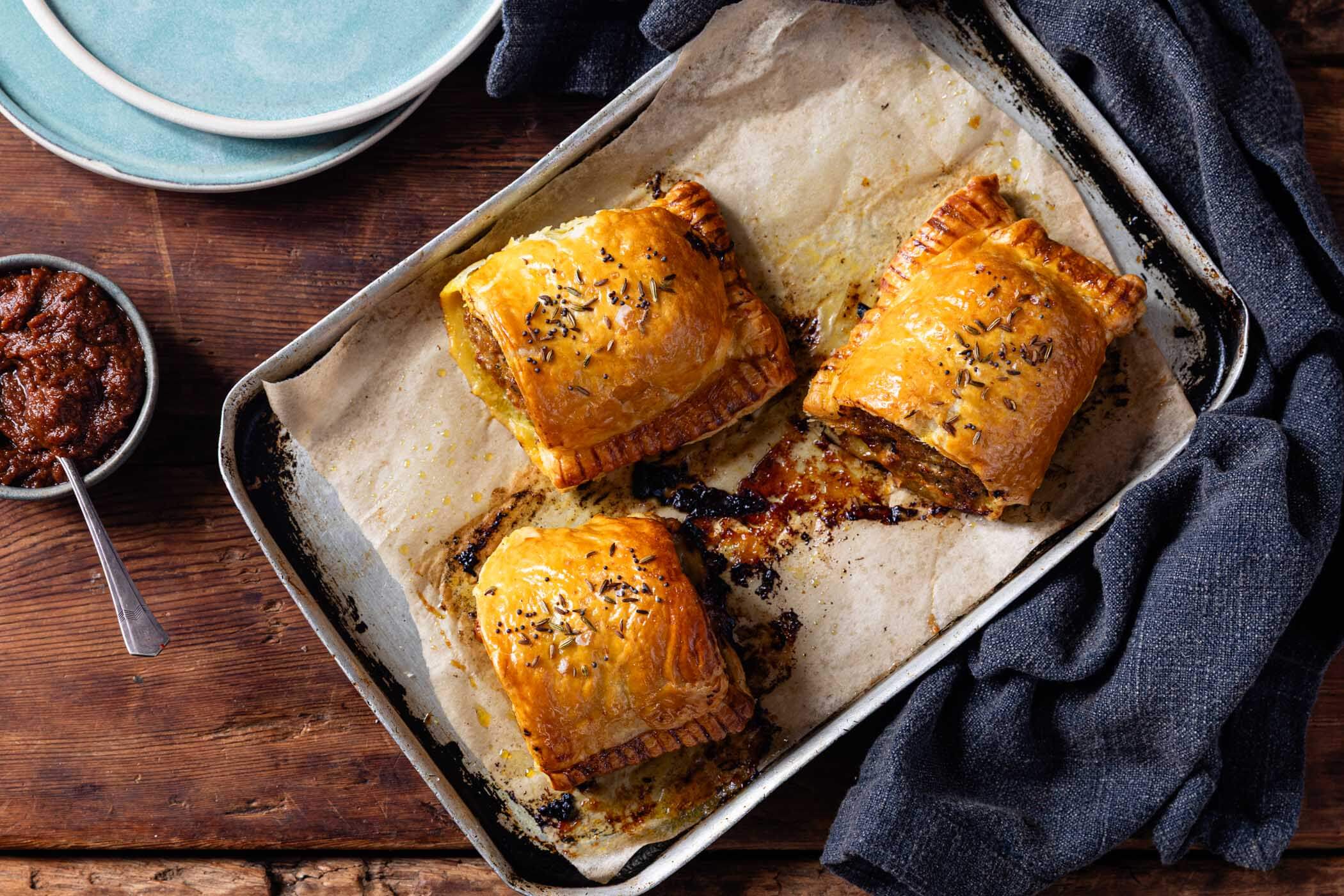 Golden curried sausage rolls freshly baked, with flaky pastry and a rich, spiced filling, served on a rustic baking tray.