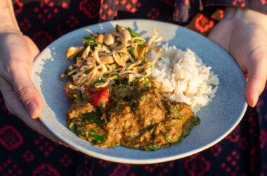 A bowl of beef rendang with jasmine rice and a side of cucumber and cabbage salad topped with roasted peanuts