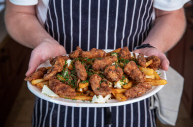 A plate of grouse and chips served poutine-style with rich gravy, golden fried grouse breasts, crispy chips, melted cheese curds and chives