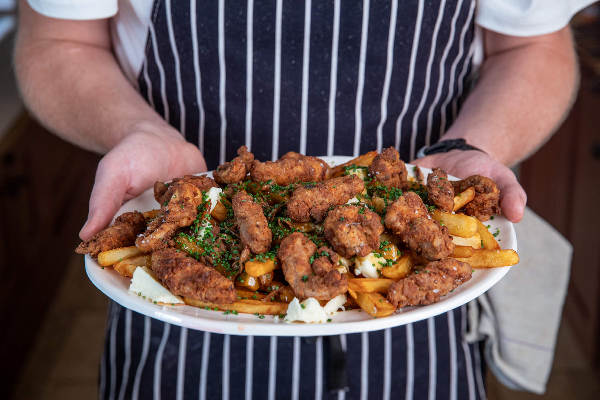 A plate of grouse and chips served poutine-style with rich gravy, golden fried grouse breasts, crispy chips, melted cheese curds and chives