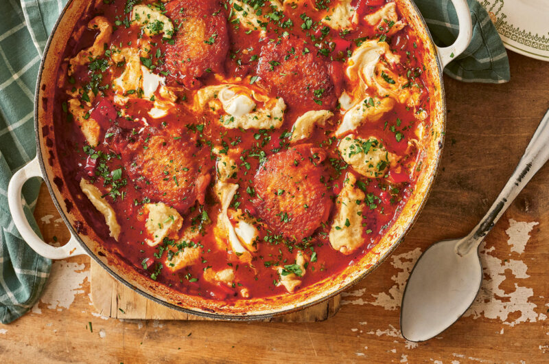Chicken paprikaš with noklice dumplings cooked in a casserole dish, topped with fresh parsley and served with sour cream