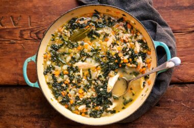 Chicken broth served in a casserole dish at the table, with cavolo nero, farro and vegetables visible