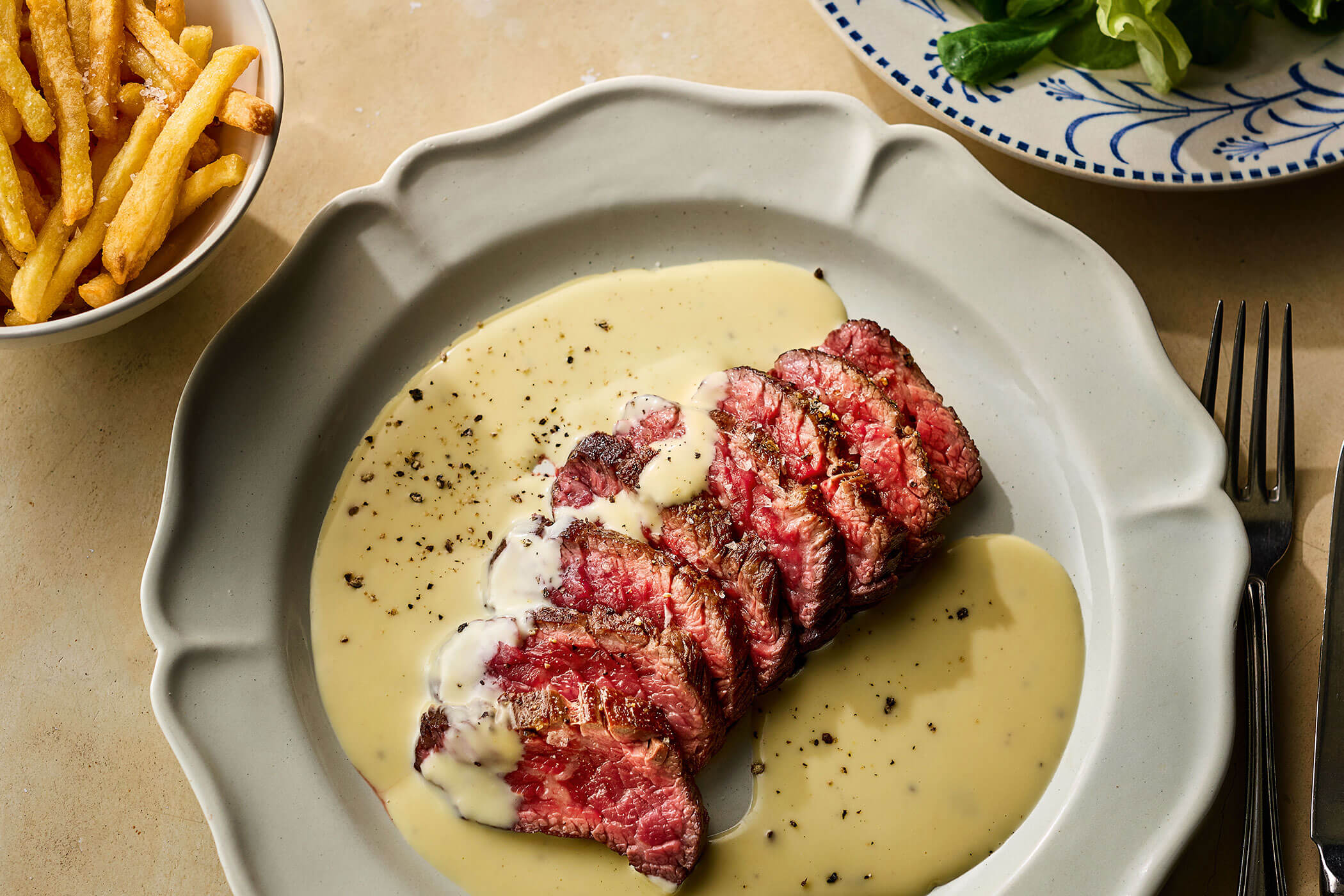 Sliced bavette steak served with Saint-Marcellin sauce and black pepper on a grey plate