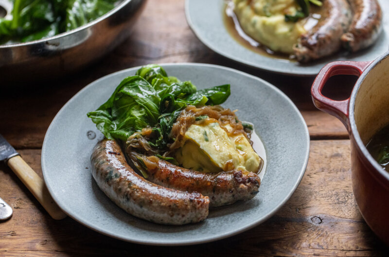 Wild garlic sausages served with champ mash, spring greens and rich onion gravy on a grey plate
