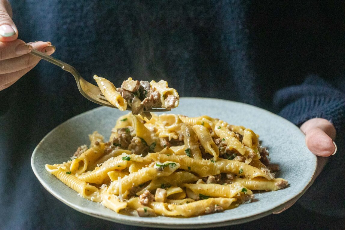 Garganelli pasta with sausage, mushrooms and cream, with a forkful lifted above the plate.