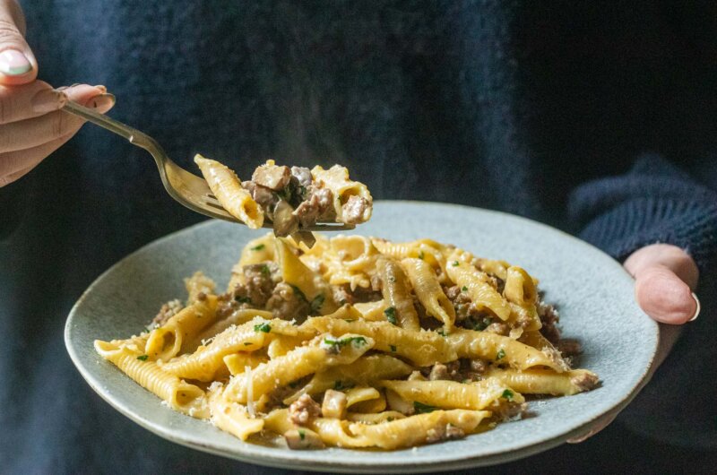 Garganelli pasta with sausage, mushrooms and cream, with a forkful lifted above the plate.